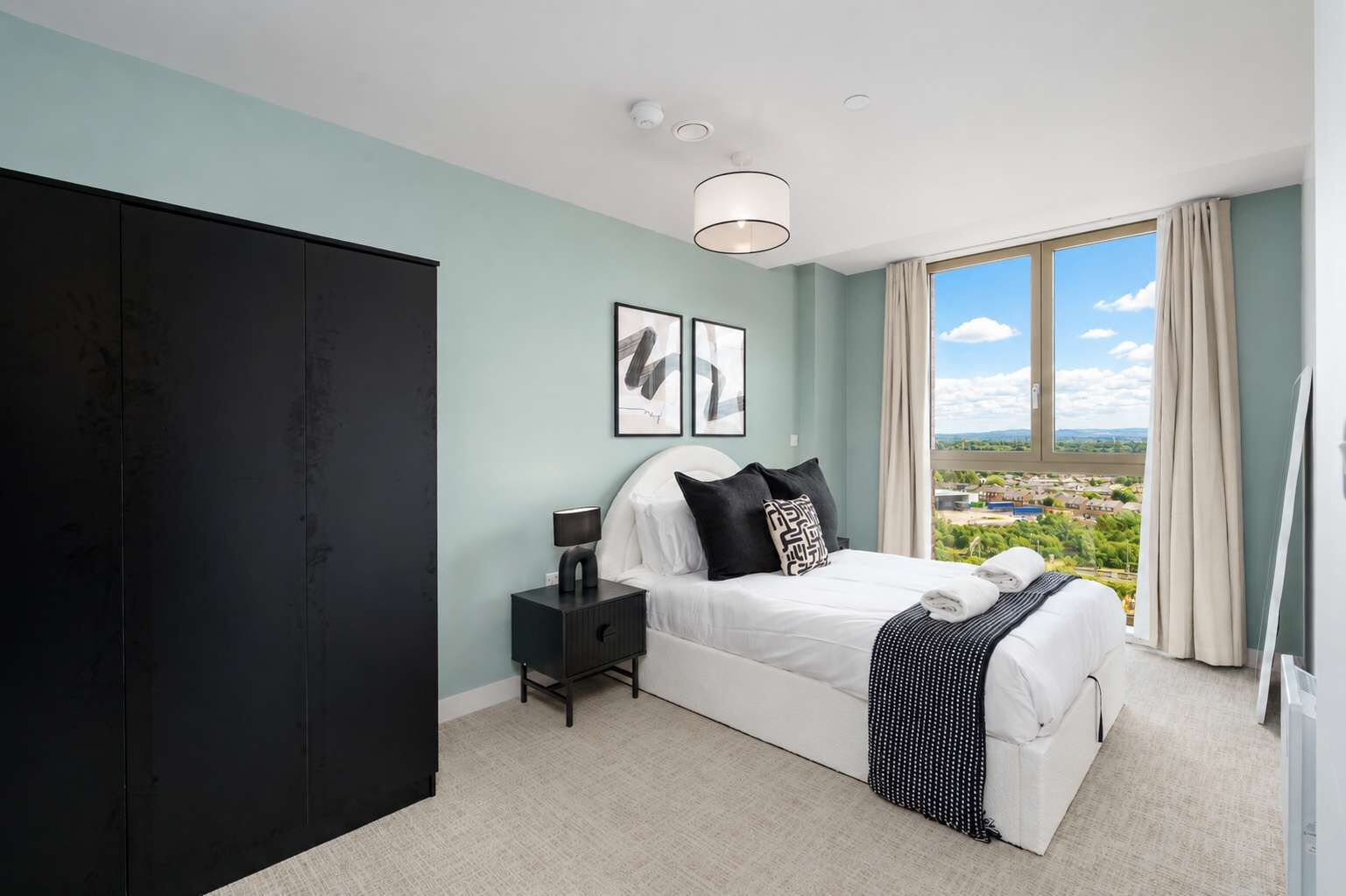 A bedroom with a bed, a nightstand, a wardrobe, and a large window with a view.