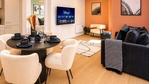 A modern living room with a dining area, a flat-screen TV mounted on the wall, and a sofa with patterned throw. - Luxury VIEWS!  10th  Floor  2 Bed Apartment (Manchester)