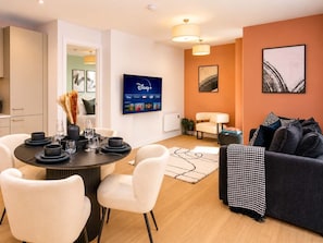 A modern living room with a dining area, a flat-screen TV mounted on the wall, and a sofa with patterned throw. - Luxury VIEWS!  10th  Floor  2 Bed Apartment (Manchester)
