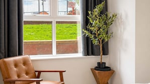 Una habitació amb finestra, una cadira, un llit i una planta en test.