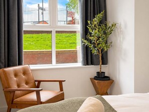 Ein Zimmer mit Fenster, einem Sessel, einem Bett und einer Zimmerpflanze.