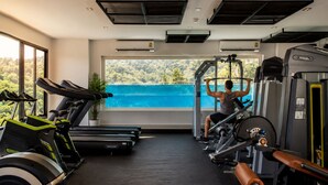 Un gimnasio con equipo de ejercicio, un ventanal con vista a una extensión de agua azul y una planta en maceta.