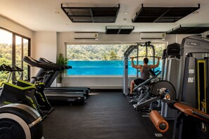 Un gimnasio con equipo de ejercicio, un ventanal con vista a una extensión de agua azul y una planta en maceta.