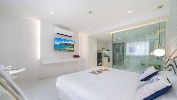 Un dormitorio moderno con una cama grande, un televisor montado y zona de ducha con paredes de vidrio.