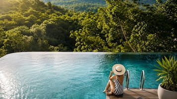 Une personne assise au bord d’une piscine, avec vue sur un paysage boisé.