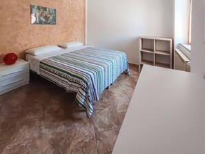 Ein Schlafzimmer mit einem Bett, einem Nachttisch, einem roten Gegenstand und einem weißen Tisch.