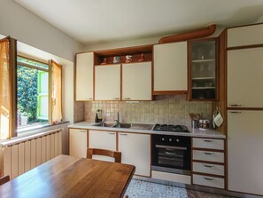 Eine kleine Küche mit Esstisch, Einbau-Schränken, Herd und einem Fenster mit Vorhängen.