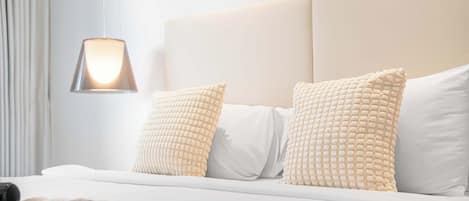 Et hotelværelse med seng, puder, lampe og dyne.