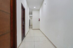 Un pasillo con paredes blancas, una puerta de madera y un extintor fijado a la pared.