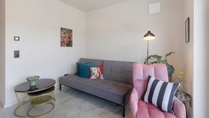 Ein modernes Wohnzimmer mit einem grauen Sofa, einem pinken Sessel, einem runden Tisch mit einer Schale und einer Stehlampe.