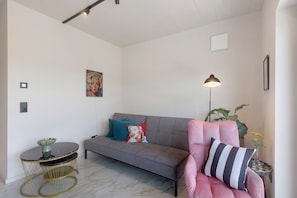 A modern living room with a grey sofa, a pink armchair, a round table with a bowl, and a floor lamp.