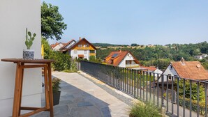 Ein Balkon mit einem Topf-Kaktus, einem Holztisch und einem Steinweg, der zu Häusern mit roten Ziegeldächern führt.