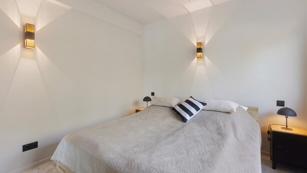 Ein Schlafzimmer mit einem Bett, zwei Nachttischen, einer Ablage und Wandleuchten.
