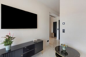 Un soggiorno moderno con una grande TV a schermo piatto montata a parete, un mobile TV nero, una pianta in vaso e un tavolino con piano in marmo.