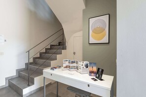 A modern interior with a staircase, a desk with brochures, and a framed abstract artwork. - Harma City Living - Terrace Maisonette (Chania)