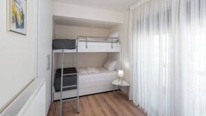 Une chambre avec un lit superposé, un radiateur, une petite table de chevet avec une lampe et une fenêtre avec des rideaux légers.