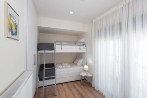 Ein Schlafzimmer mit Etagenbetten, einem Heizkörper, einem kleinen Nachttisch mit Lampe und einem Fenster mit durchscheinenden Vorhängen.