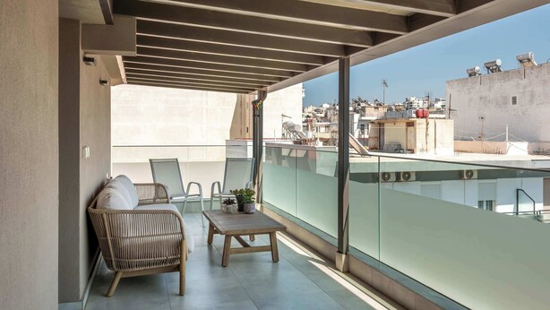 Un balcon doté d'une balustrade en verre, de meubles en osier et offrant une vue sur le paysage urbain.