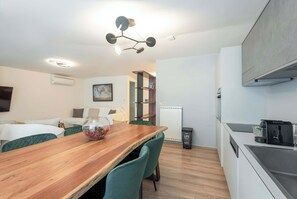 Une cuisine moderne avec une table à manger en bois, des chaises recouvertes d’un tissu vert, une machine à café et un radiateur.