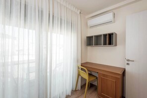 A room with a wooden desk, a yellow chair, a white air conditioning unit, and a white door. - Harma City Living - Terrace Maisonette (Chania)