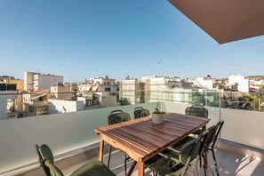 A balcony with a wooden table and chairs, overlooking a cityscape with various buildings. - Harma City Living - Terrace Maisonette (Chania)