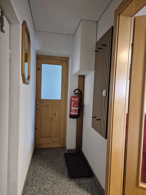 Um corredor com uma porta de madeira, um extintor fixado na parede e um tapete pequeno na entrada.