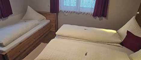 A room with two beds, a wooden headboard, a window with lace curtains, and a wall switch.