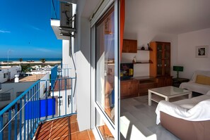 A balcony with a view of the beach, a dining area with a table and chairs, and a living room with a sofa and a TV. - Tomy Apartment – Families Only, Sea View, Balcony, Wi-Fi (Conil de la Frontera)
