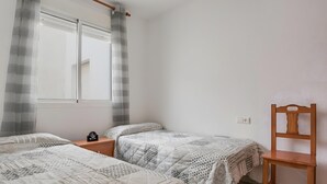 Ein Schlafzimmer mit zwei Einzelbetten, einem Holzstuhl, einem Nachttisch mit einer Uhr und einem Fenster mit Vorhängen.