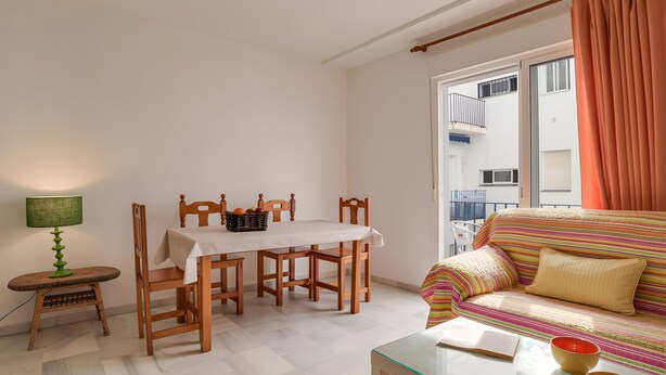 Ein Wohnzimmer mit Esstisch, Stühlen, einer Couch, einem Glastisch und einem Fenster mit Vorhängen.