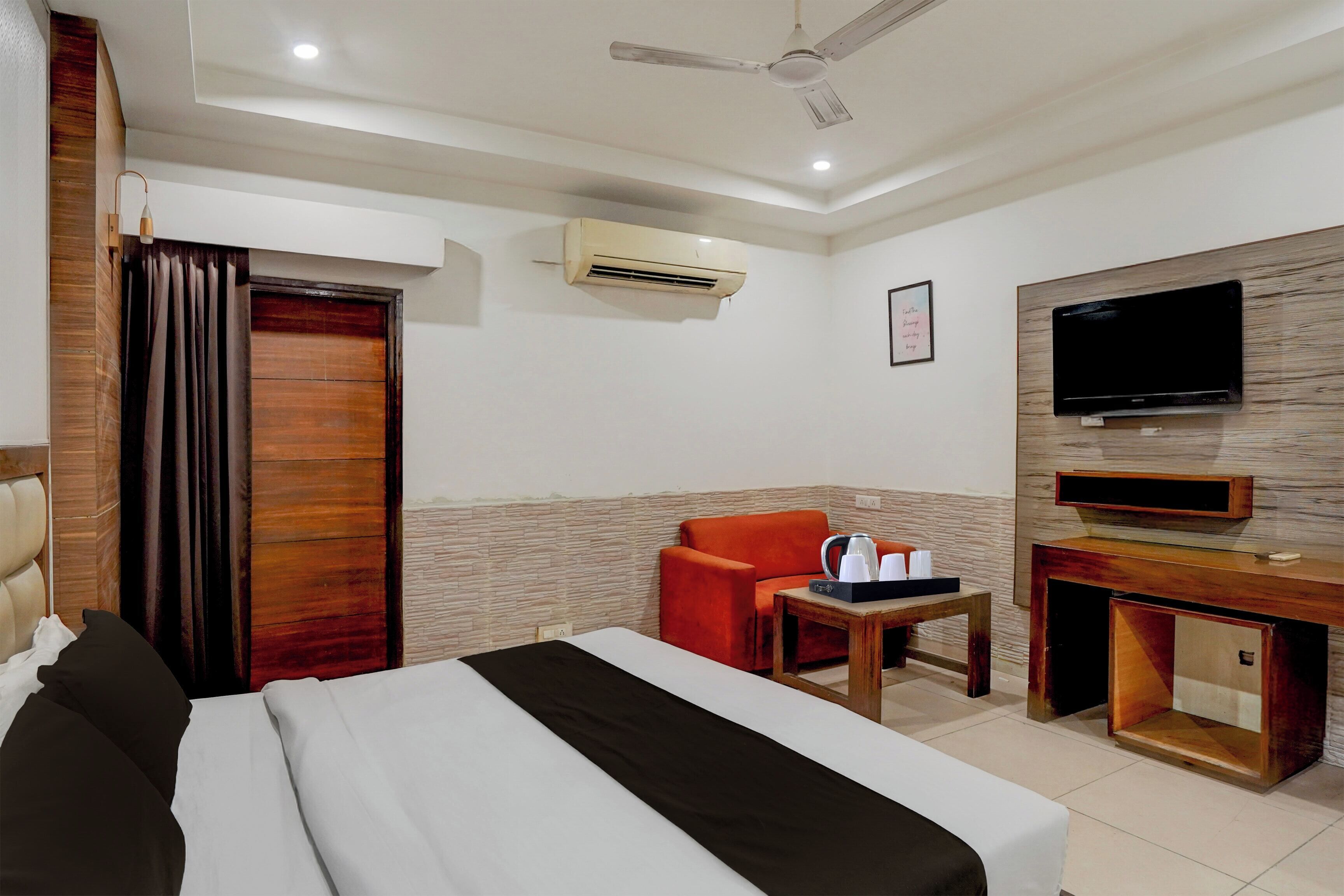 Habitación de hotel con cama, un escritorio y silla, televisor de pantalla plana, unidad de aire acondicionado y ventilador de techo.