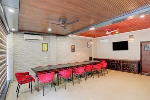 A conference room with a long table, red chairs, a ceiling fan, and a mounted television. - Super Townhouse by Zirakpur Bus Stand (Zirakpur)