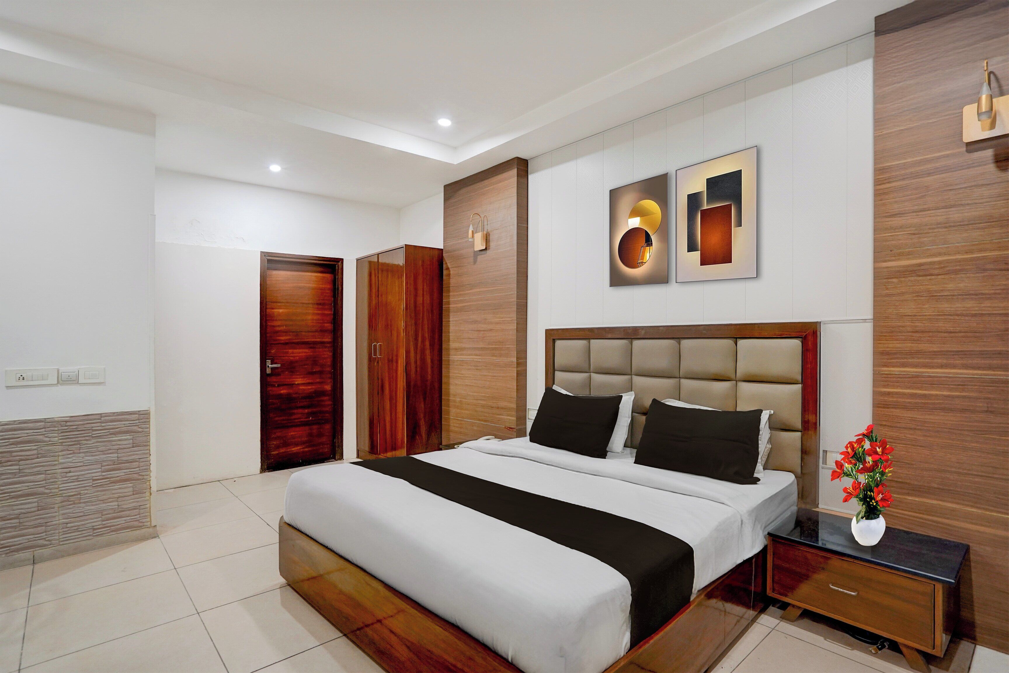 A modern bedroom with a large bed, a nightstand, a wall-mounted lamp, and a decorative piece above the bed.