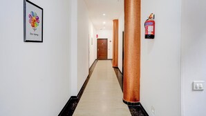 Een hotelgang met een ingelijst kunstwerk, een brandblusser en een deur aan het einde.