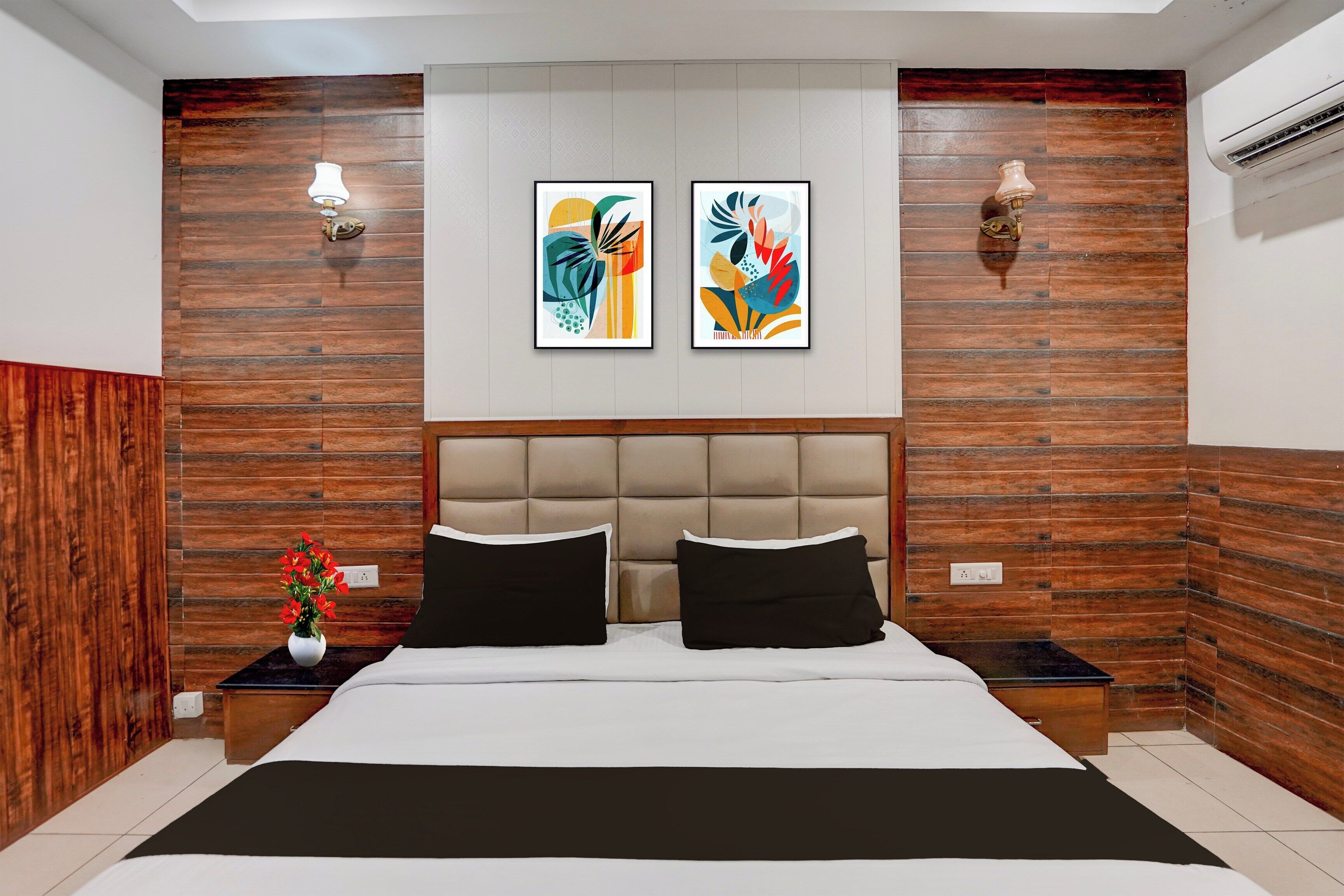 Un dormitorio con una cama grande, dos lámparas fijadas a la pared y dos cuadros abstractos enmarcados.
