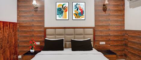 A bedroom with a large bed, two wall-mounted light fixtures, and two framed abstract paintings.