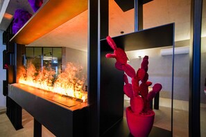Un intérieur moderne agrémenté d’une cloison en verre, d’un foyer et d’une sculpture représentant un cactus.