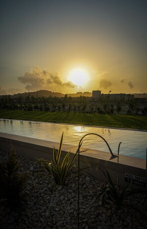 A swimming pool with a view of a sunset and distant buildings. - Luxury Countryside Retreat with Pool, Spa & Gym (Zebbug)