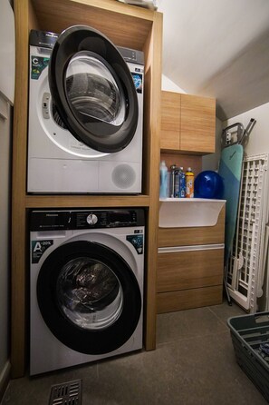 A compact laundry room with two stacked washing machines, a sink, and a drying rack.