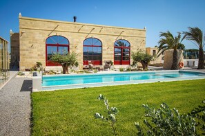 A modern building with a swimming pool, large arched windows, and outdoor seating.