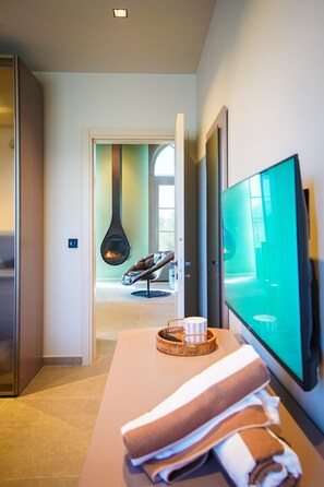 Une chambre d’hôtel moderne dotée d’une télévision à écran plat, d’une cheminée, d’un fauteuil confortable et d’une table avec des serviettes.