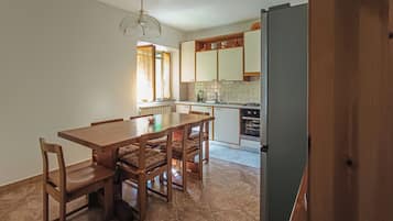 A compact kitchen with a dining area, including a table and chairs, a refrigerator, and a window with curtains.