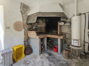 A stone-built fireplace with a chimney, a water heater, and a red bucket on the floor. - Il Rifugio di Anna (Tresana)