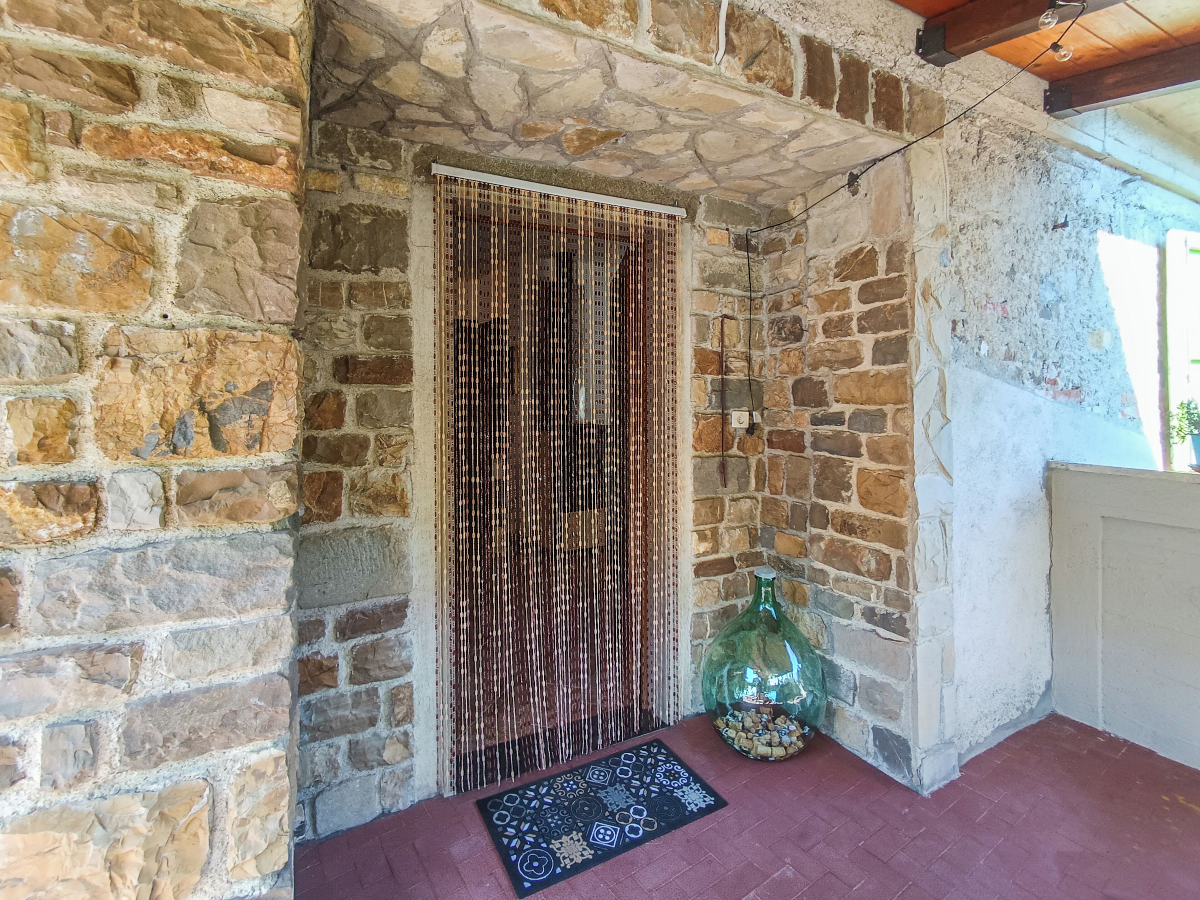 A stone-walled room with a patterned rug, a decorative bottle, and a hanging light fixture.