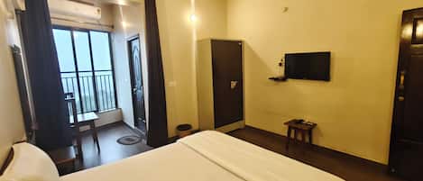 A hotel room with a bed, a TV mounted on the wall, a door, and a balcony with a view.