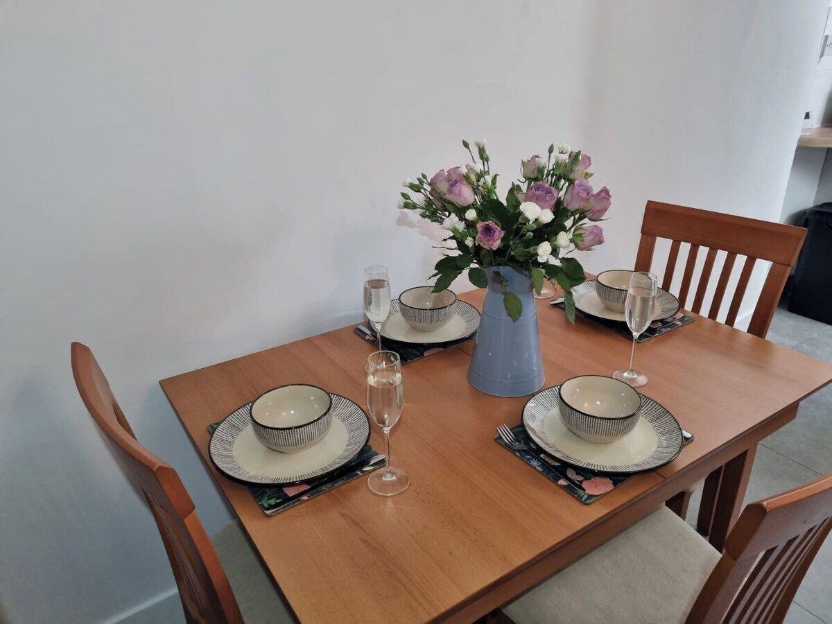 Une table à manger dressée avec des assiettes, des bols et des verres, agrémentée d’un vase de fleurs.