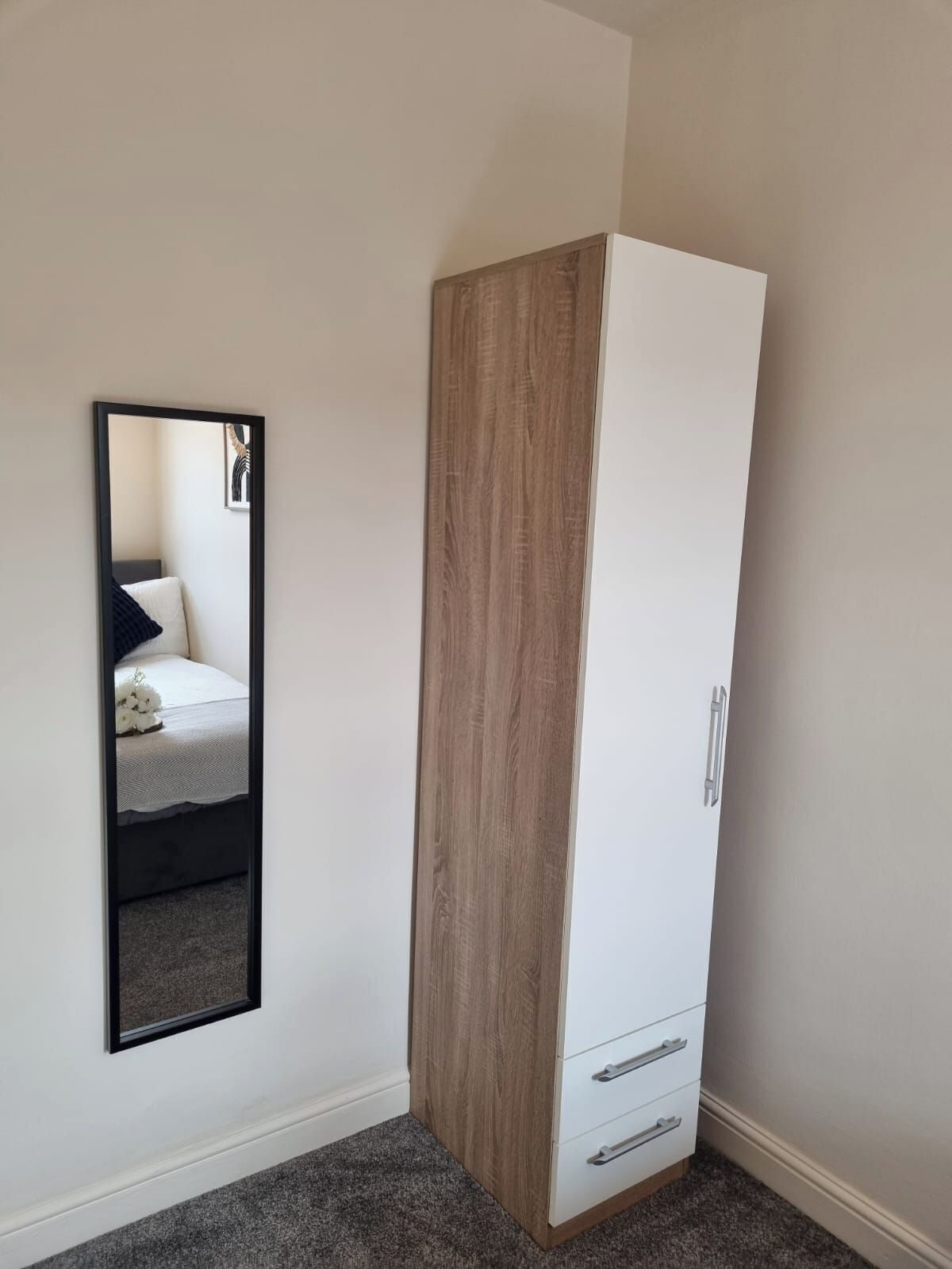 A room with a wardrobe, a mirror, and a bed.