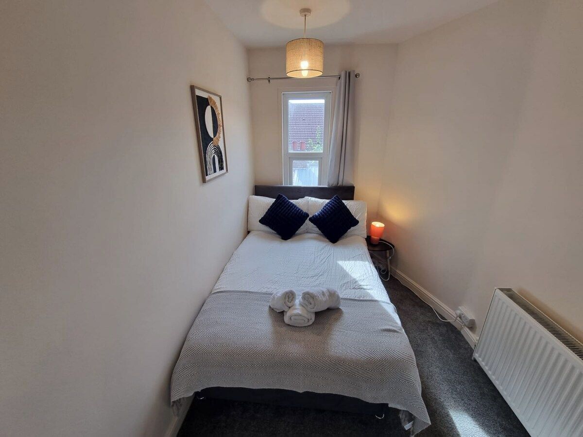 A small, narrow hotel room with a single bed, a bedside table with a lamp, and a radiator.