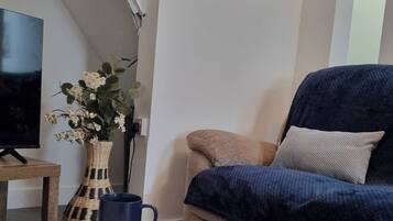 Un salon avec un canapé, une horloge murale, un téléviseur, un vase de fleurs et une bougie posée sur une table.