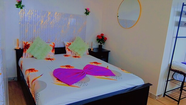 A bed with floral bedding, a bedside table with a vase of flowers, and a round mirror on the wall. - Hotel splanada poilon (Assomada)